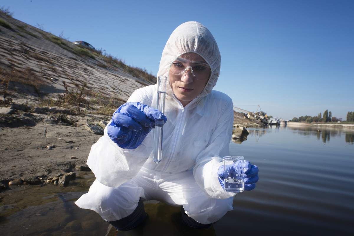 Una persona experta en medio ambiente toma una muestra de agua de un río
