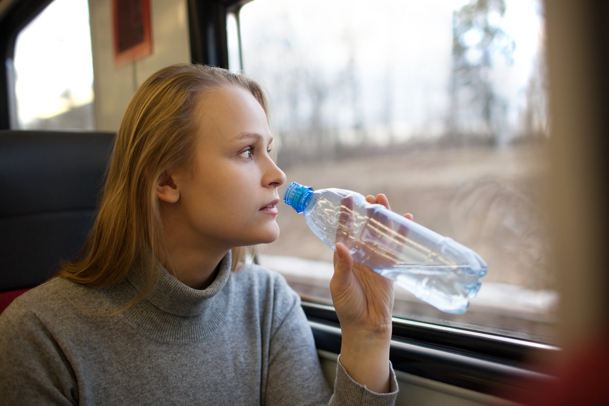 Passenger drinking water from a bottle on a train and looking out of the window